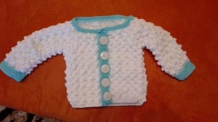 Weiße gehäkelte Babyjacke mit türkisfarbener Einfassung und fünf Knöpfen, flach ausgelegt