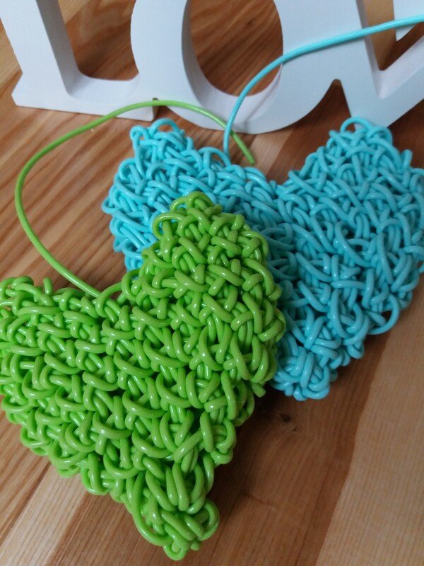 Gehäkelte grüne und türkise Herzen aus Kordel auf Holzboden vor weißen Dekobuchstaben