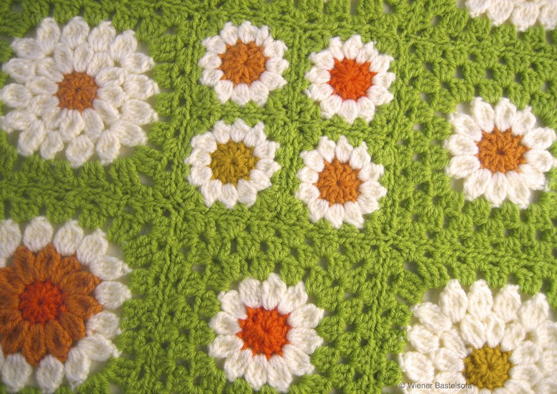 Verbundenes Granny‑Motiv mit weißen Blüten und orange‑gelben Zentren auf grünem Häkelgrund