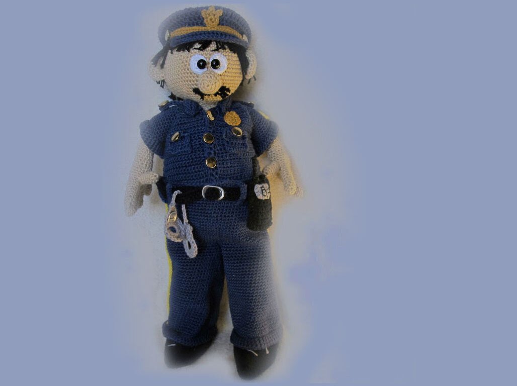 Hand-crocheted amigurumi doll wearing a navy police uniform with cap, belt, badge and small handcuff accessory