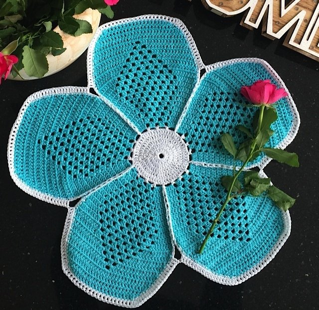 Gehäkeltes türkis-weißes Deckchen in Blumenform mit weißem Zentrum und einer rosa Rose darauf