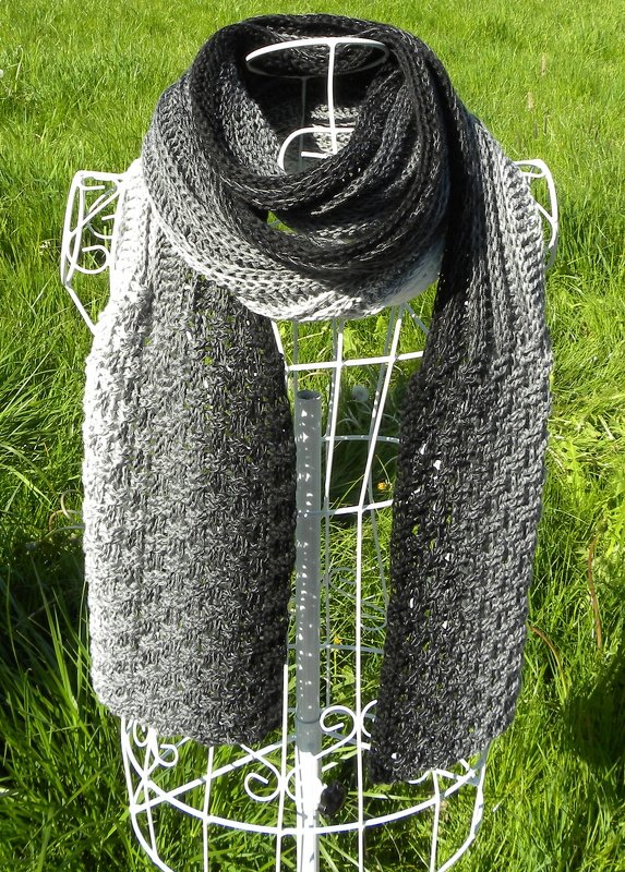Gehäkelter Schal mit Grau‑Schwarz‑Verlauf auf weißer Büste vor grünem Gras