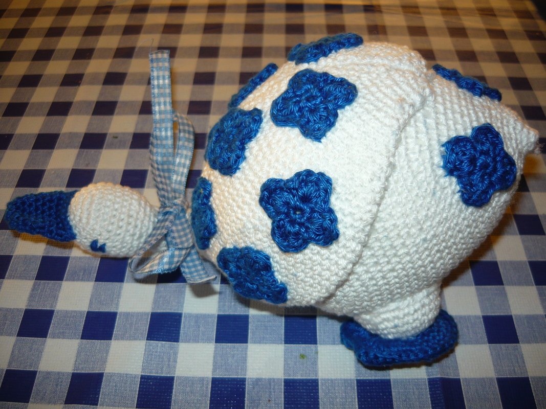 weiß-blauer gehäkelter Amigurumi-Vogel mit blauen Blumenapplikationen und kariertem Band