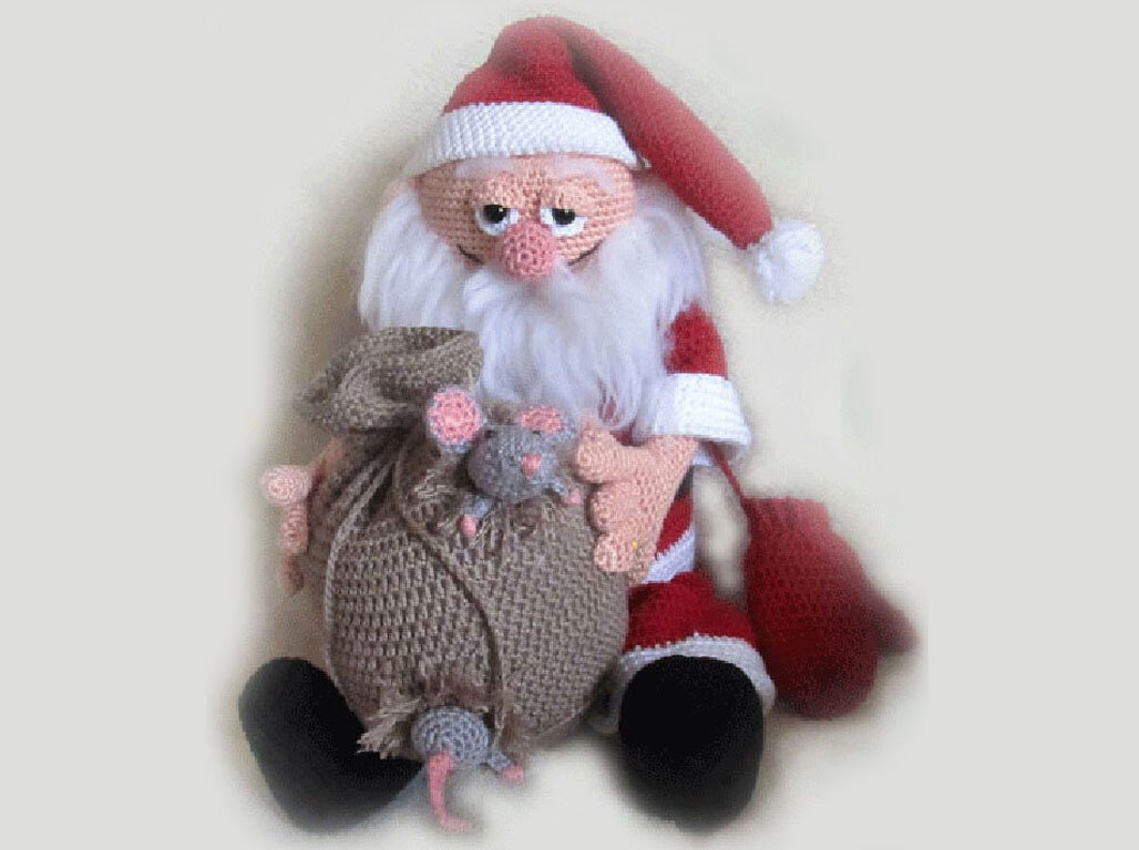 Seated crocheted Santa Claus doll in a red suit and long hat holding a brown sack with two small gray mice.
