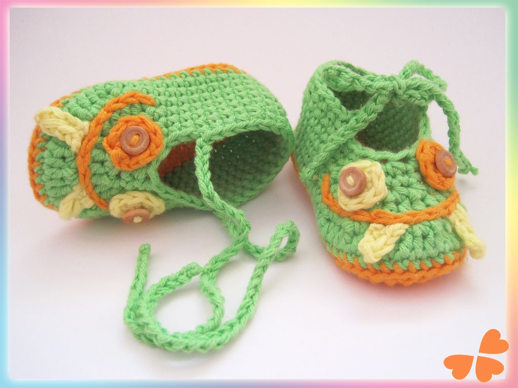 Gehäkelte Babyschuhe in Hellgrün mit orange-gelben Applikationen und kleinen Knöpfen auf weißem Hintergrund.