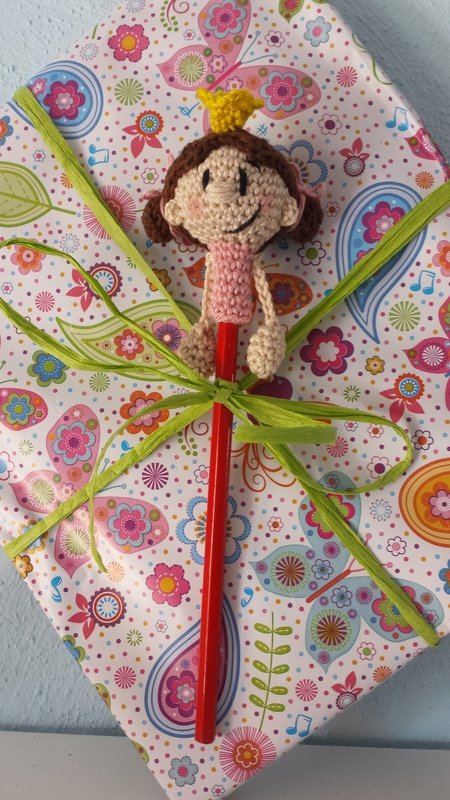 Amigurumi-Prinzessin aus Häkelgarn mit gelber Krone auf rotem Stift, dekorativ an Geschenk gebunden
