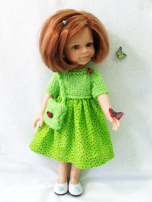 Doll wearing a short-sleeve green knitted top, a green polka-dot skirt, and a small knitted bag with a ladybug accent.