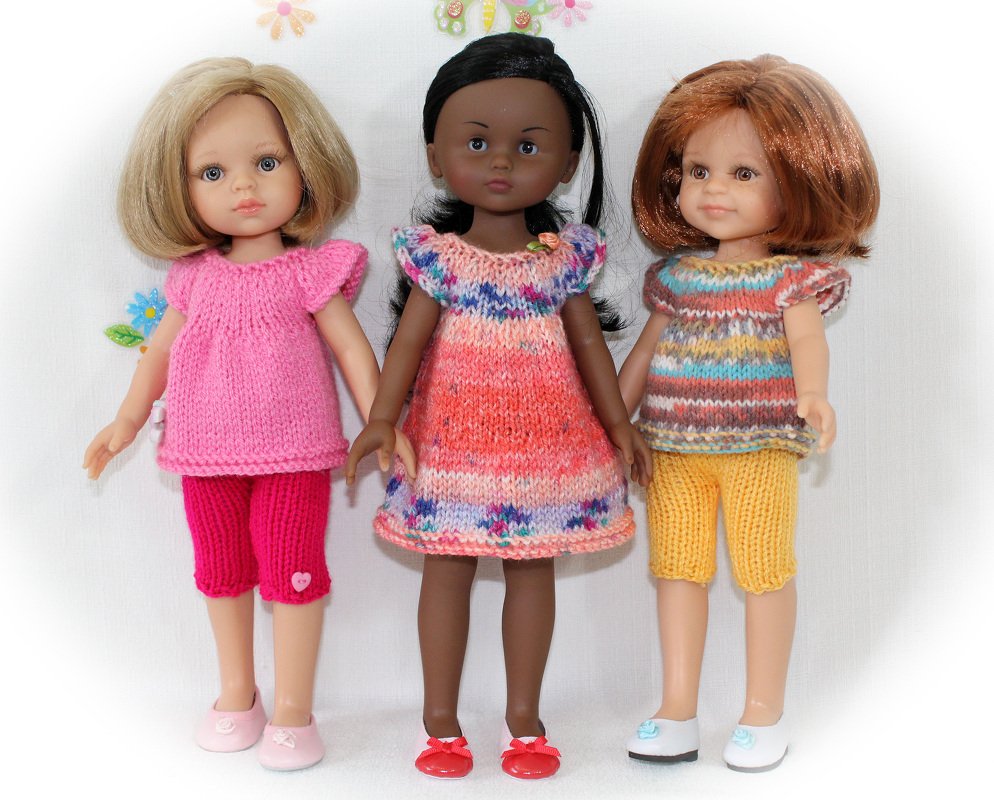 Three dolls in knitted outfits: pink top with pants, multicolored dress, and striped top with yellow pants.