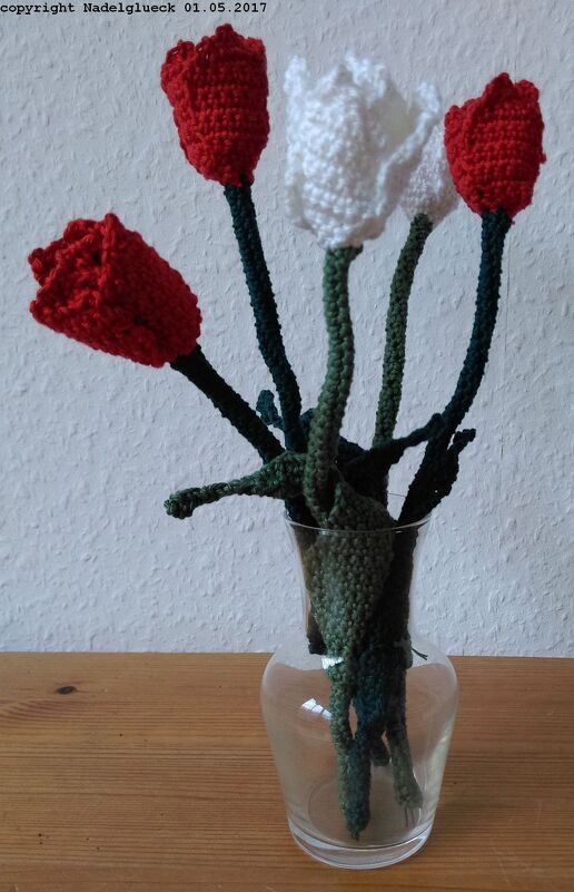 Fünf gehäkelte Tulpen (drei rot, zwei weiß) in einer klaren Glasvase auf einer Holzoberfläche