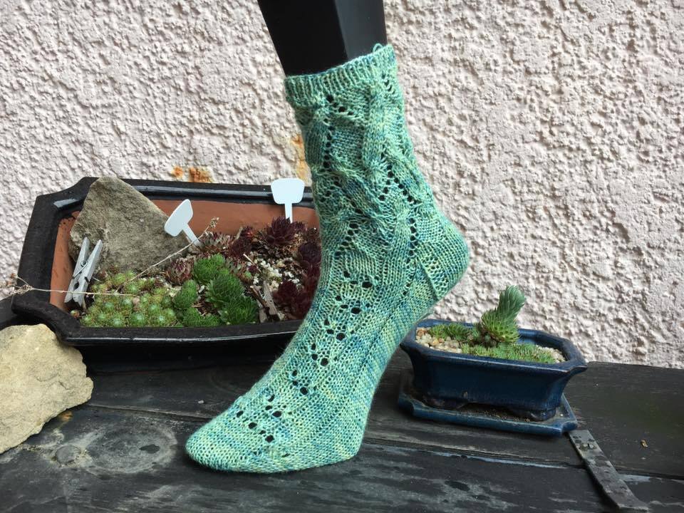 Nahaufnahme einer grünen gestrickten Ankle-Socke mit Ajour- und Zopfmuster auf einem Fußmodell