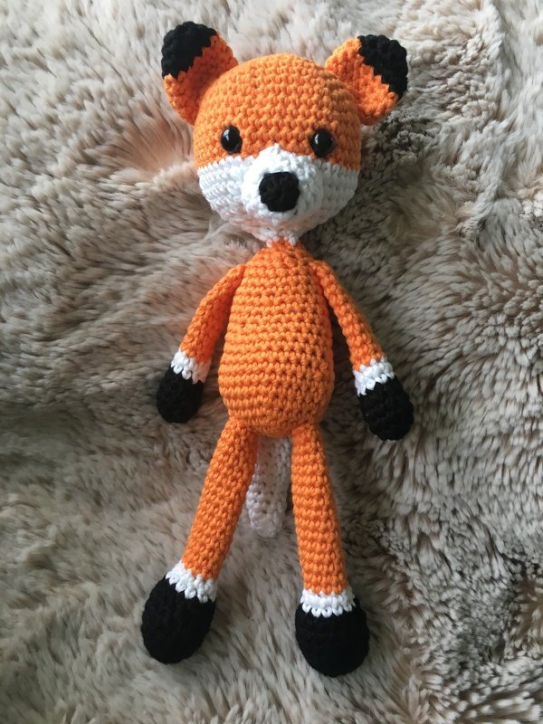 Gehäkelter orange-weißer Fuchs mit schwarzen Details auf hellbraunem, flauschigem Untergrund