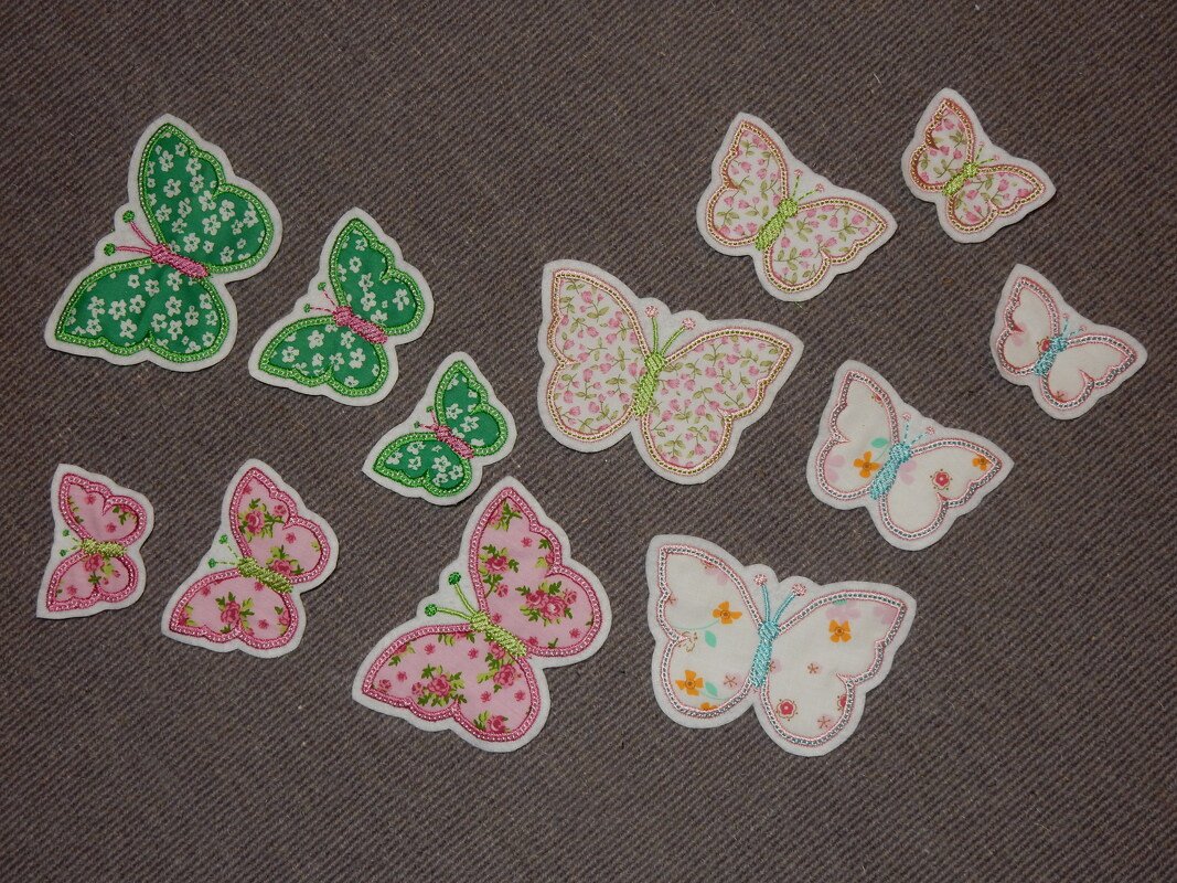 Bestickte Schmetterlings-Applikationen mit floralen Mustern in Grün, Pink und Weiß auf dunklem Stoff