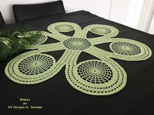 Hellgrüner gehäkelter Tischläufer mit Spiral- und Kreisdesign auf dunklem Tisch.