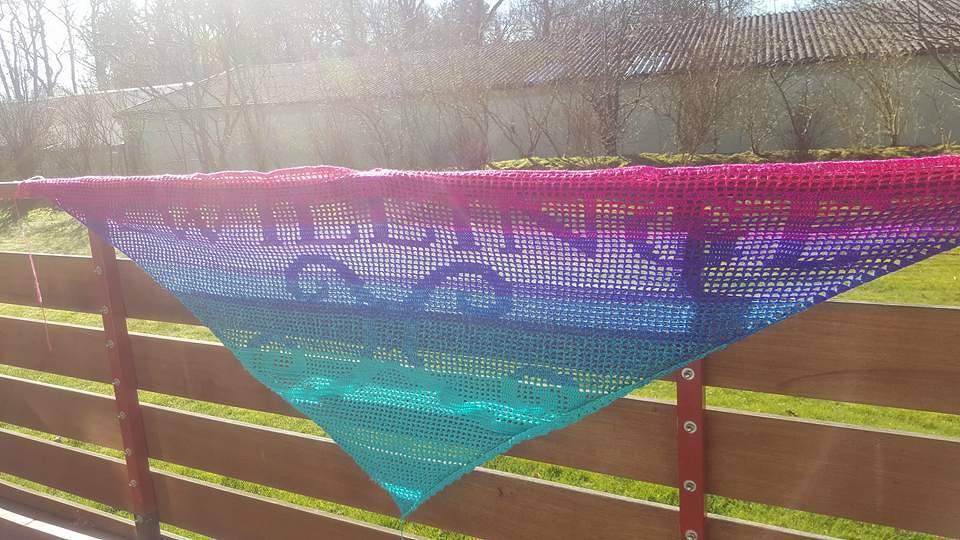 Gehäkeltes Dreieckstuch in Pink-Lila-Blau-Türkis mit eingearbeitetem Schriftzug „KILLING IT GOOD“ an einem Holzzaun.