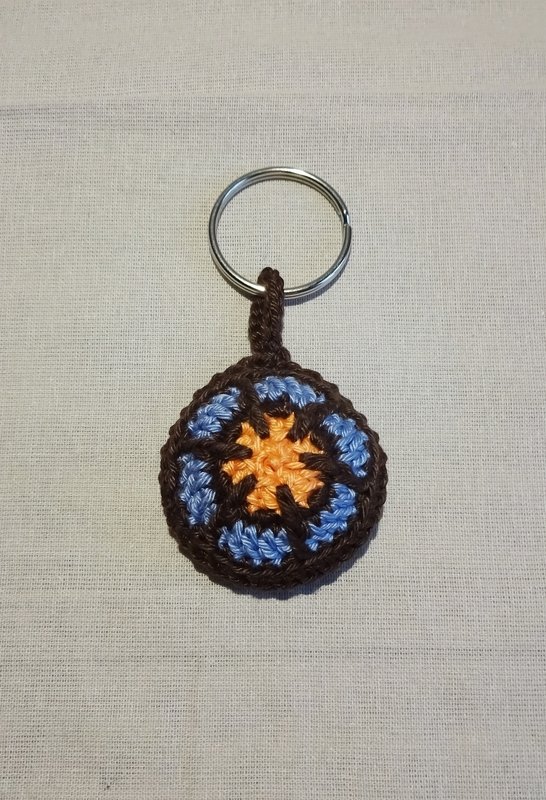 Runder gehäkelter Schlüsselanhänger in Braun, Blau und Orange mit sternförmigem Muster und Metallring