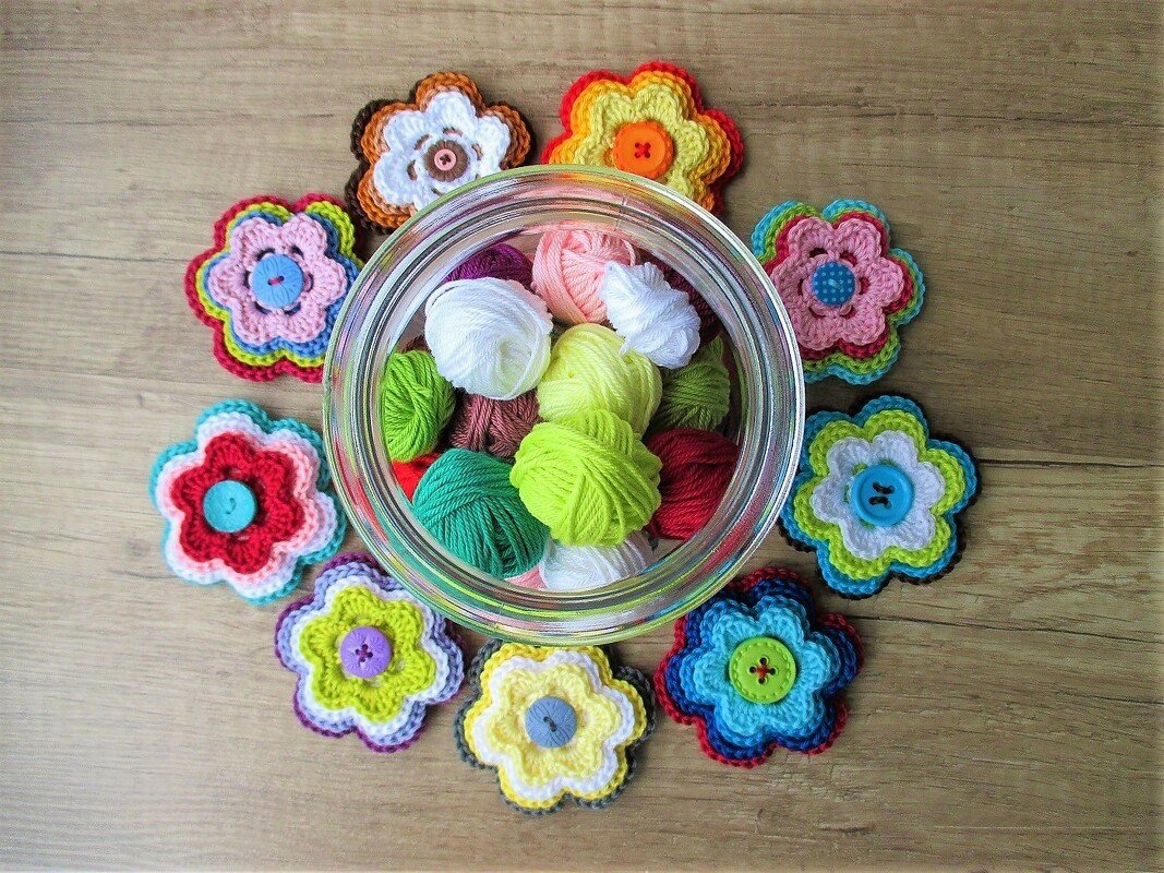 Bunte gehäkelte Blumenapplikationen mit Knöpfen um ein Glas mit Garn