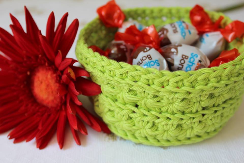Limettengrüner gehäkelter Korb mit verpackten Bonbons neben roter Gerbera