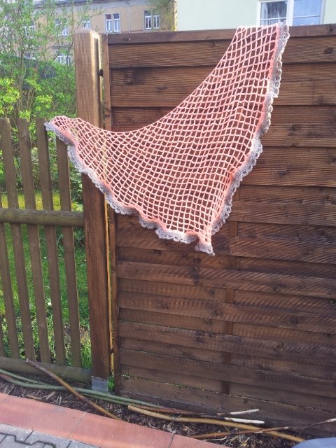 Rosa gehäkeltes Dreieckstuch mit grauer Wellenborte, an einem Holzzaun hängend