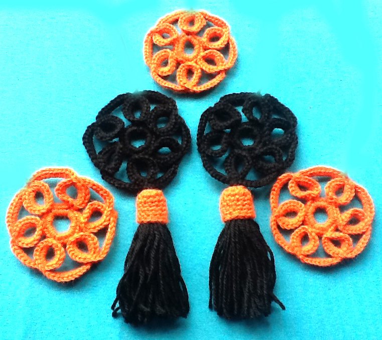 Vier orange und zwei schwarze gehäkelte Kreisornamente sowie zwei schwarze Quasten mit orangener Kappe auf blauem Hintergrund