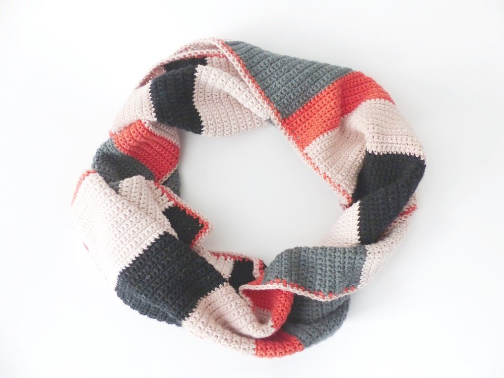 Gehäkelter Loop-Schal in Beige, Grau und Koralle mit Farbblockmuster auf weißem Hintergrund