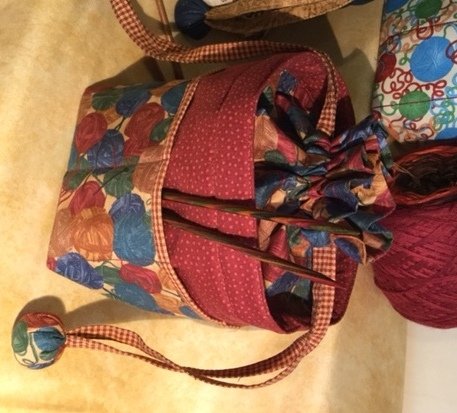 Stofftasche mit buntem Wollknäuel-Muster, rotem gepunktetem Futter und Stricknadeln