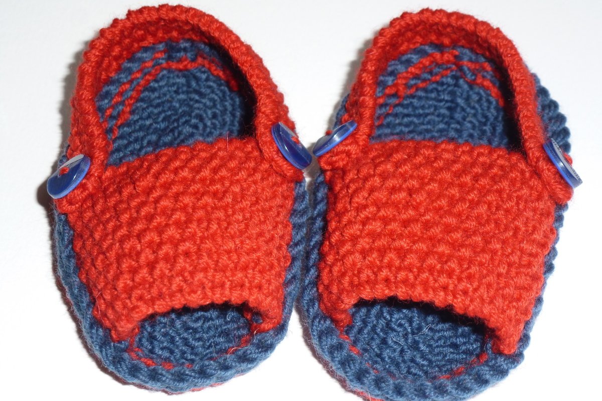 Obenansicht handgestrickter zweifarbiger Babyschuhe in Rot und Dunkelblau mit seitlichen blauen Knöpfen