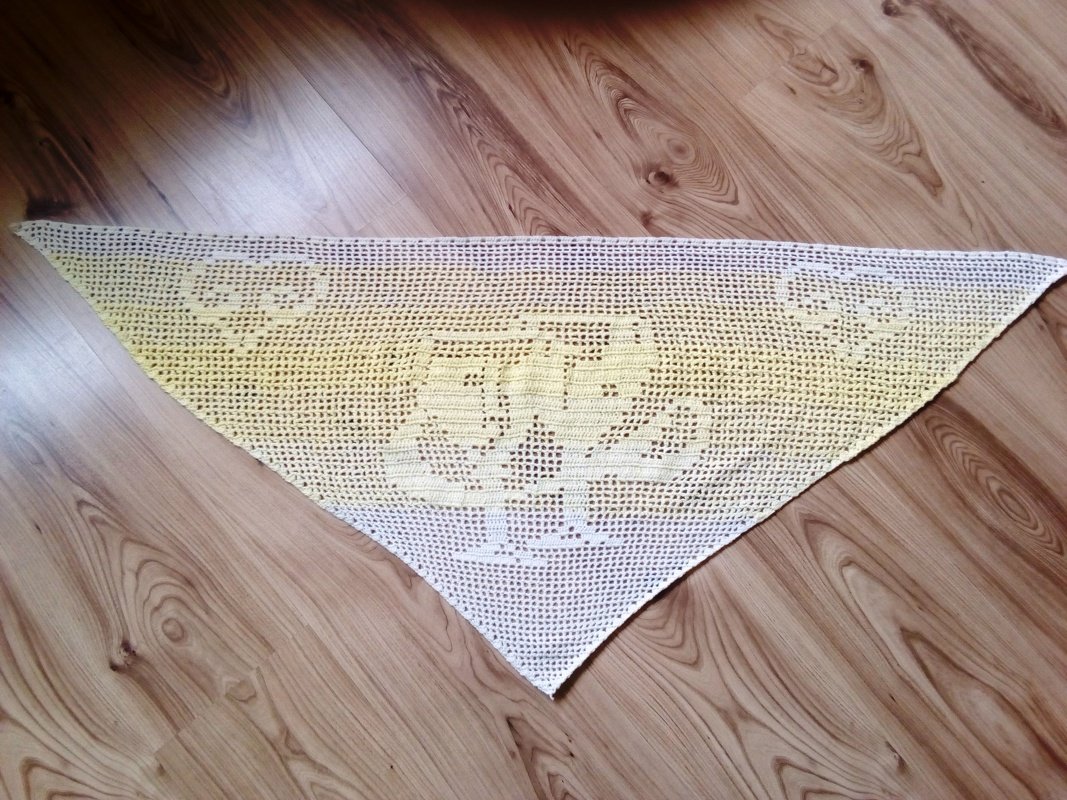 Gehäkeltes dreieckiges Tuch mit Weiß‑Gelb‑Farbverlauf und Schafmotiv auf Holzfußboden