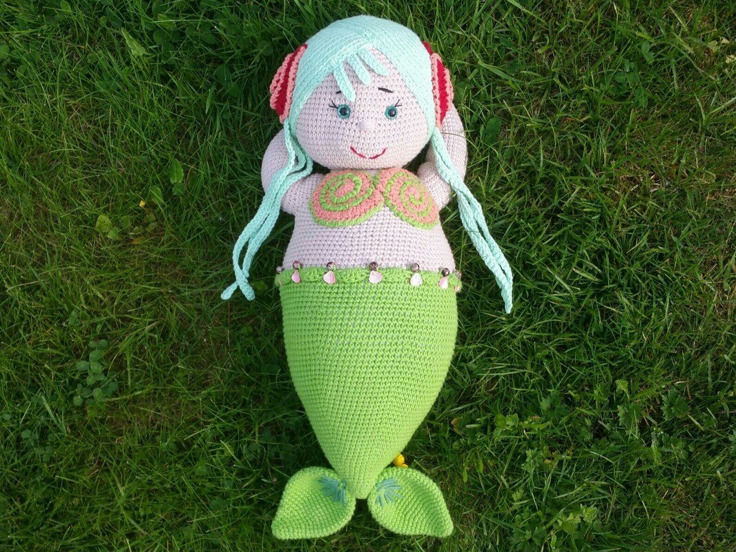 Handgehäkelte Amigurumi-Meerjungfrau mit hellgrünem Schwanz und mintgrünen Haaren auf Gras