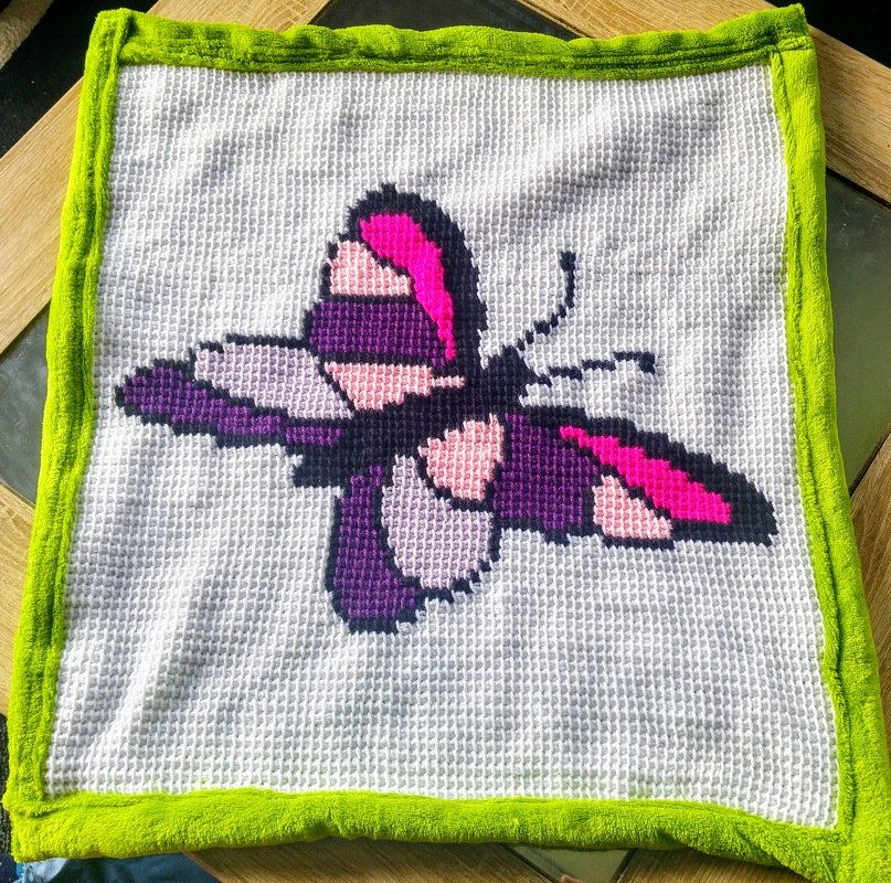 Weiße gehäkelte Babydecke mit lila-rosa Schmetterling und grünem Rand