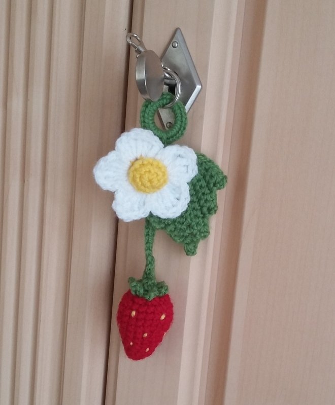 Gehäkelter Schlüsselanhänger mit weißer Blume, grünem Blatt und roter Erdbeere an einem Schlüsselring.