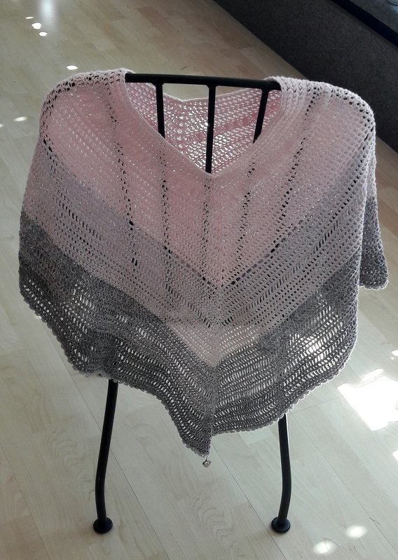 Gehäkelter dreieckiger Poncho in Rosé und Grau, über einer Stuhllehne drapiert