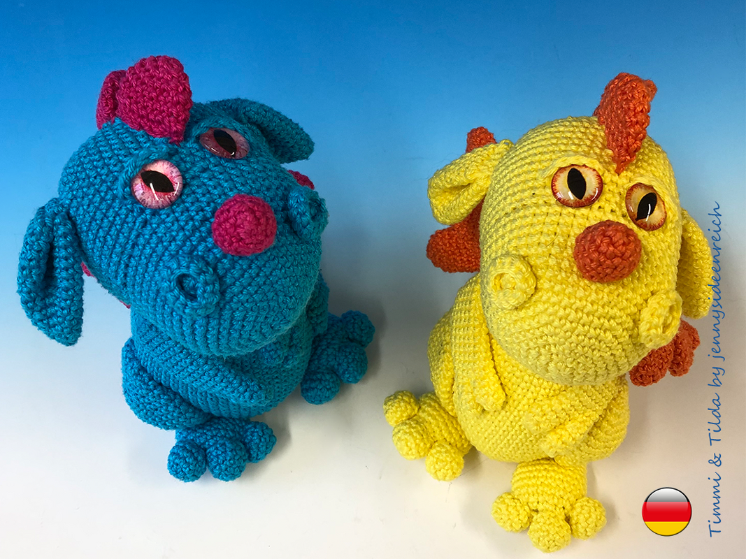 Zwei gehäkelte Amigurumi-Drachen, einer blau mit pinken Akzenten, einer gelb mit orangefarbenen Akzenten