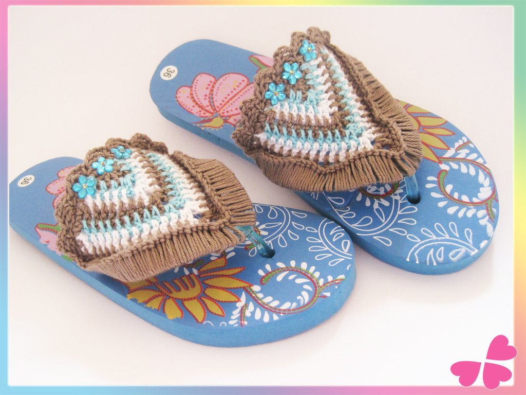 Zwei blaue Zehenstegsandalen mit gehäkelten braun-weiß-türkisen Riemen und Blumenmuster auf der Sohle