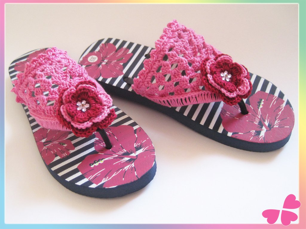 Paar Flip-Flops mit rosa Häkelriemen und mehrlagiger Blüte auf gestreifter, floral bedruckter Sohle