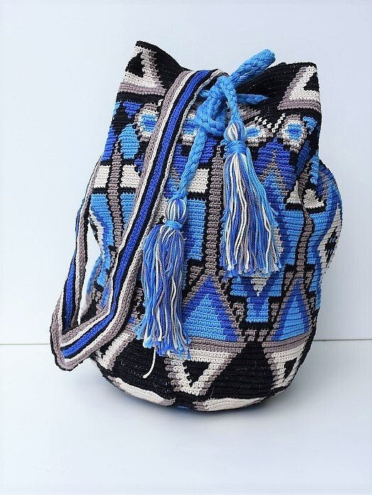 Gehäkelte Umhängetasche in Blau, Schwarz und Grau mit geometrischem Muster und Quasten vor weißem Hintergrund.