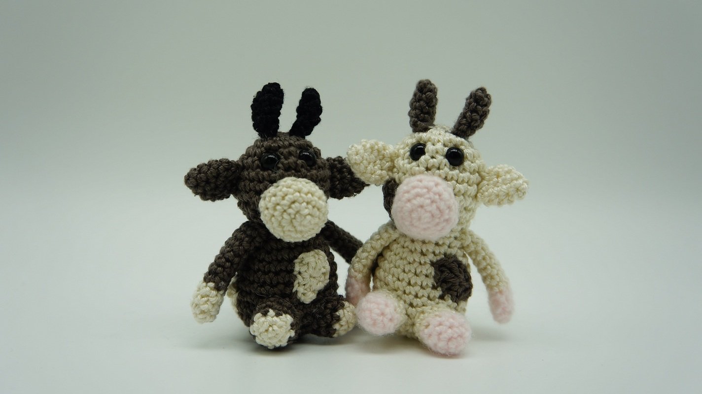 Zwei handgehäkelte Amigurumi-Kühe, eine braun, eine beige.