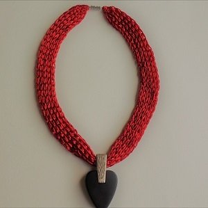 Rote gestrickte Halskette mit schwarzem Herzanhänger auf hellem Hintergrund