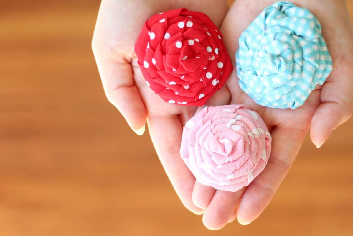 Drei Mini-Stoffrosen in Rot, Rosa und Hellblau in einer Hand