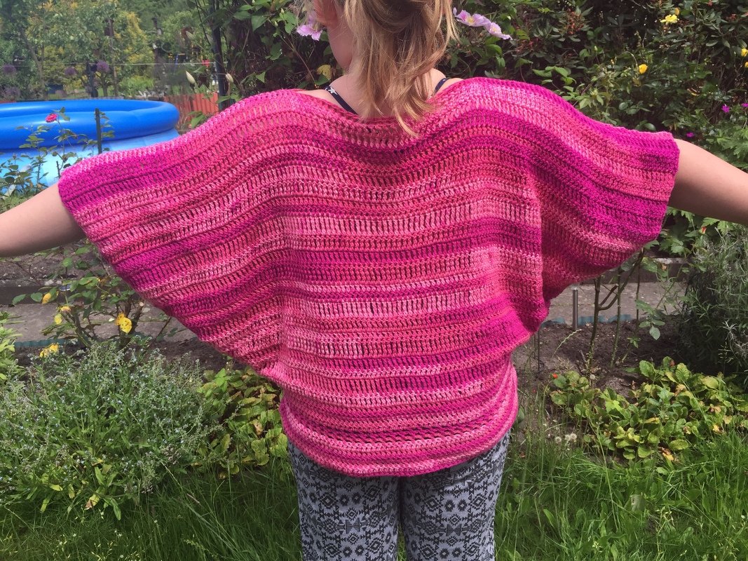 Rückansicht eines Kindes in locker sitzendem, pink-gestreiftem Häkelpullover mit Fledermausärmeln im Garten