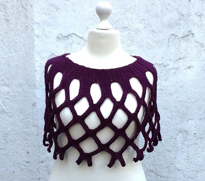 Dunkellila gehäkeltes Poncho-Oberteil mit großem Netzmuster auf Schaufensterpuppe.