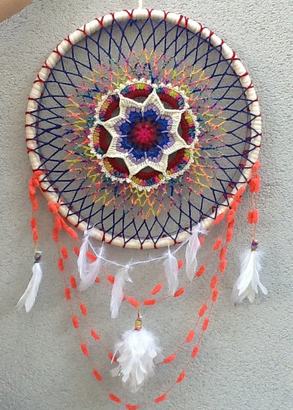 Gehäkelter Traumfänger mit buntem Mandala, dunkelblauem Netz, weißen Federn und orangen Kordeln.