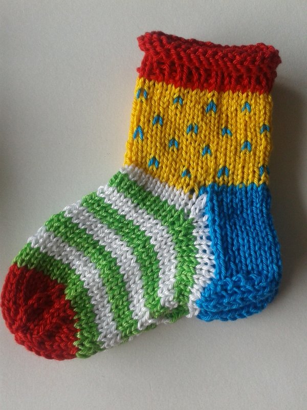 Small knitted baby sock with red cuff, yellow leg with blue eyelets, blue heel, green-and-white striped foot and red toe
