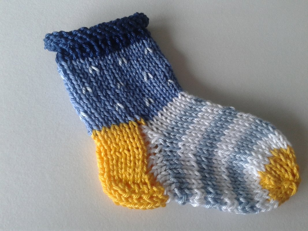 Small knitted baby sock with variegated blue-and-white foot, yellow heel and toe, and dark blue rolled cuff
