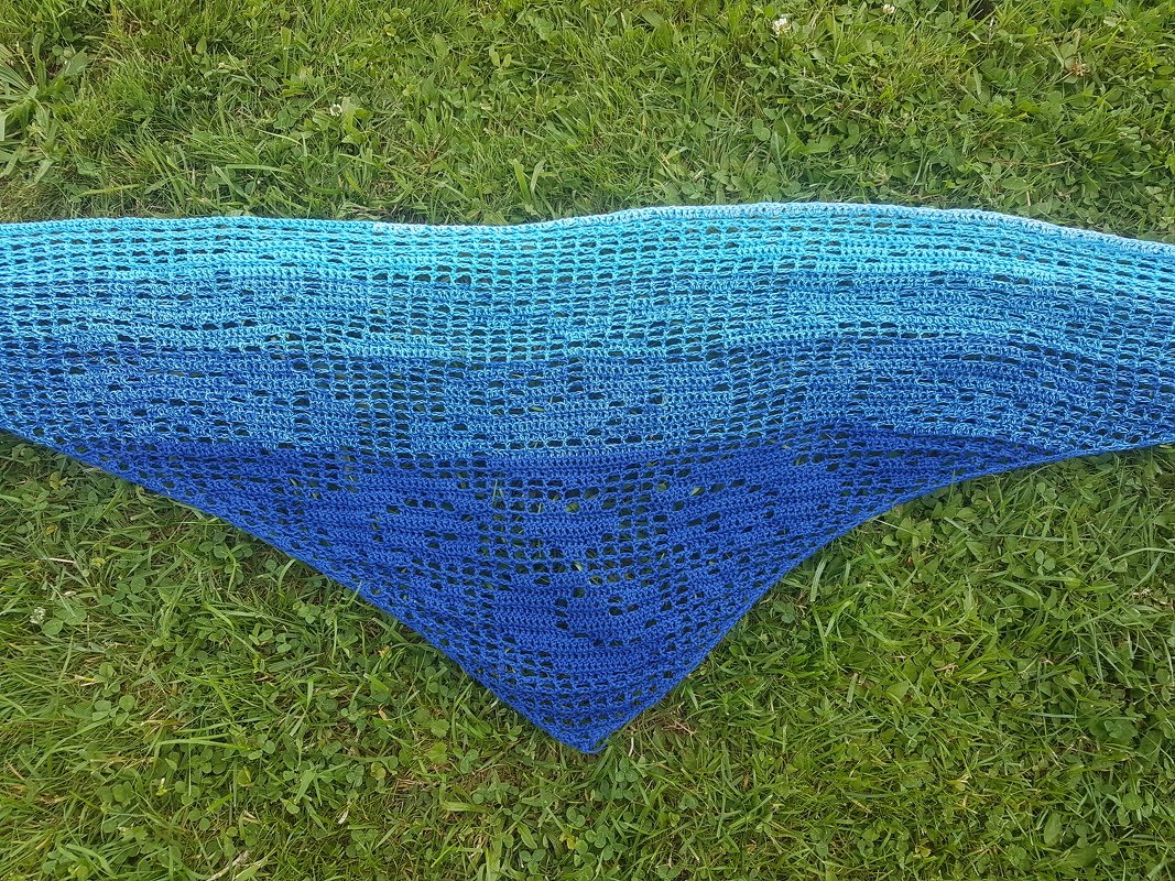 Gehäkeltes dreieckiges Tuch mit Netzmuster und Motiv, Farbverlauf von Türkis zu Blau, ausgebreitet auf Gras