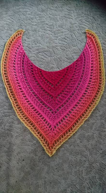 Gehäkeltes Dreieckstuch mit Farbverlauf Pink–Orange–Gelb und offenem Spitzenmuster auf grauem Untergrund