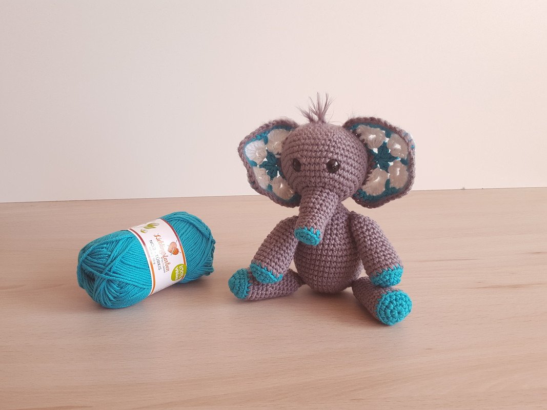 Grau-türkis gehäkelter Amigurumi-Elefant sitzend neben einem Garnknäuel