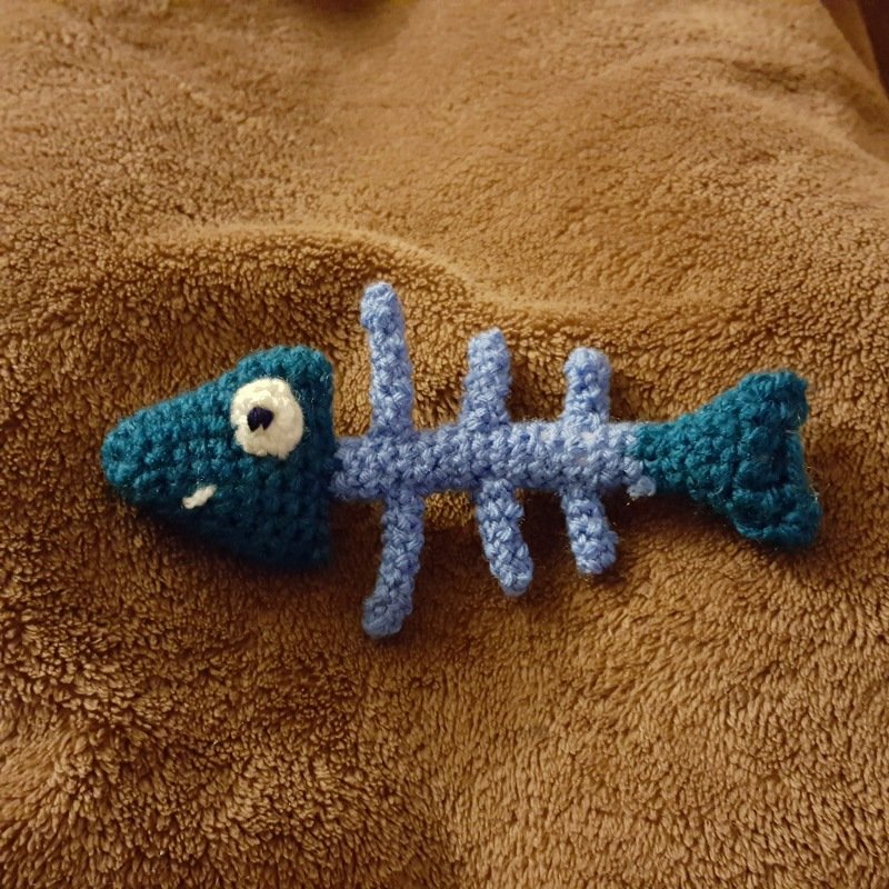 Handgehäkeltes Fischskelett-Katzenspielzeug in Blau- und Türkistönen auf brauner Decke