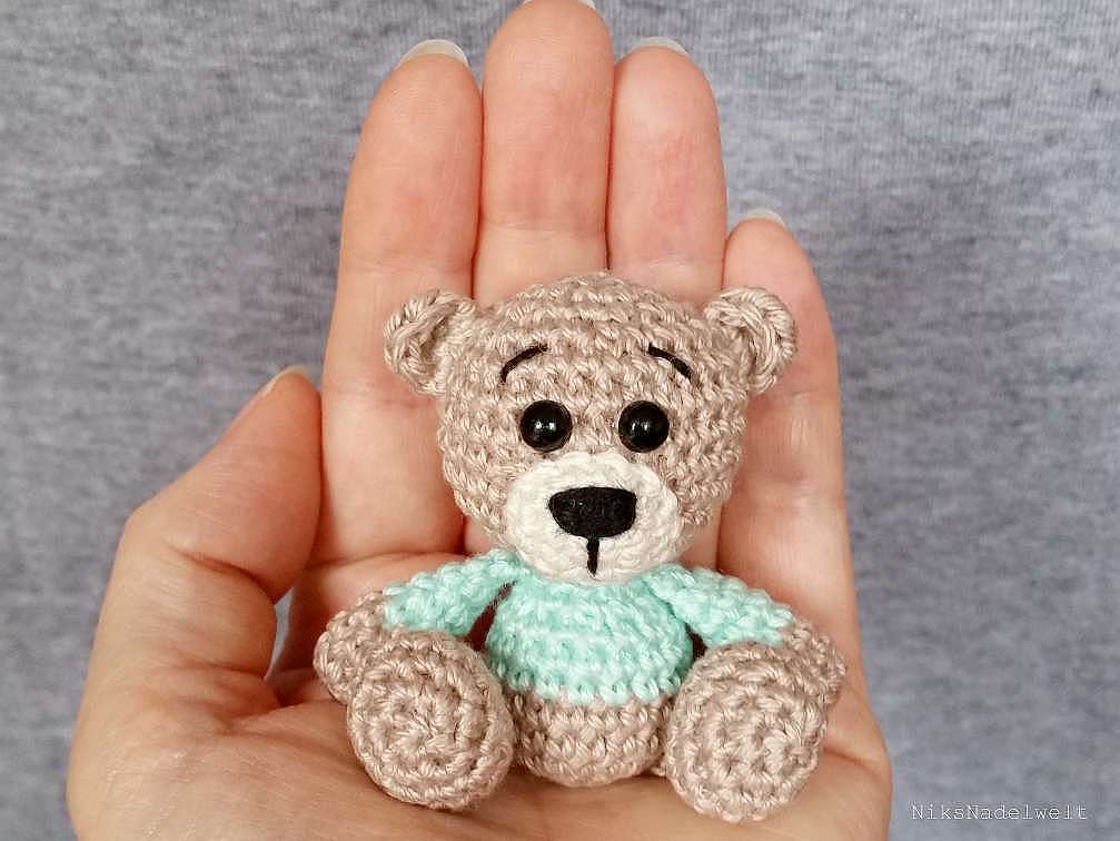 Kleiner gehäkelter Amigurumi-Teddy mit mintgrünem Pullover liegt in einer Hand
