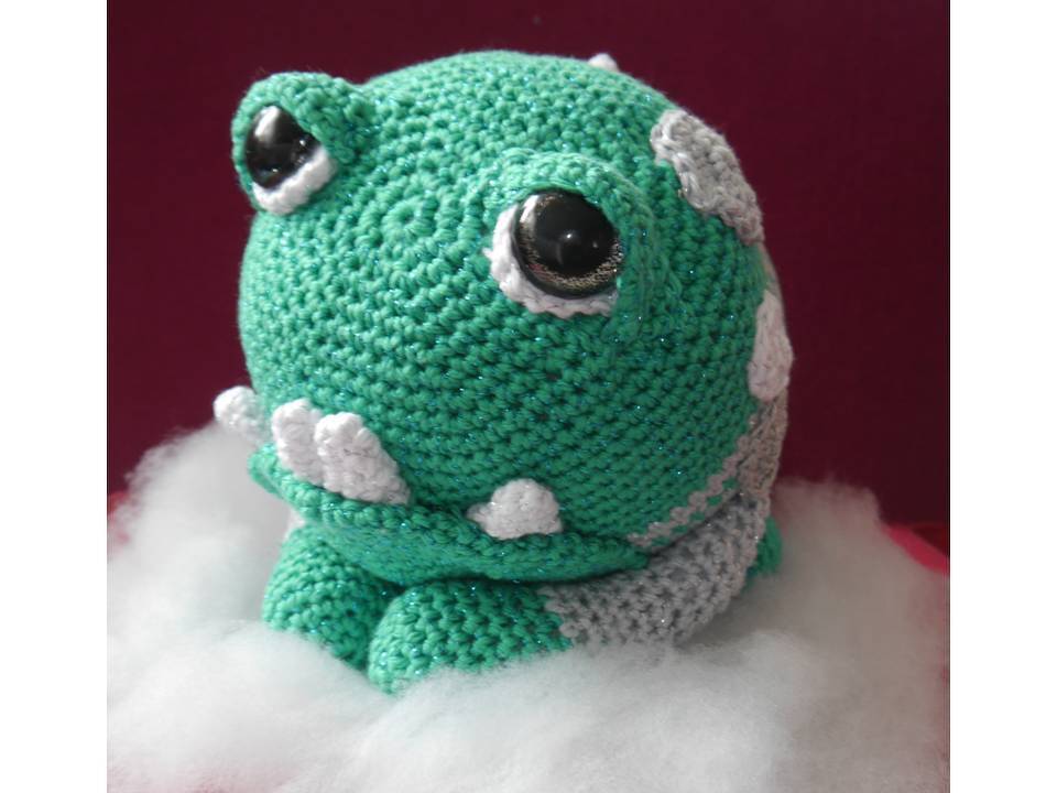 Grünes und graues gehäkeltes Amigurumi mit weißen Tupfen und schwarzen Sicherheitsaugen