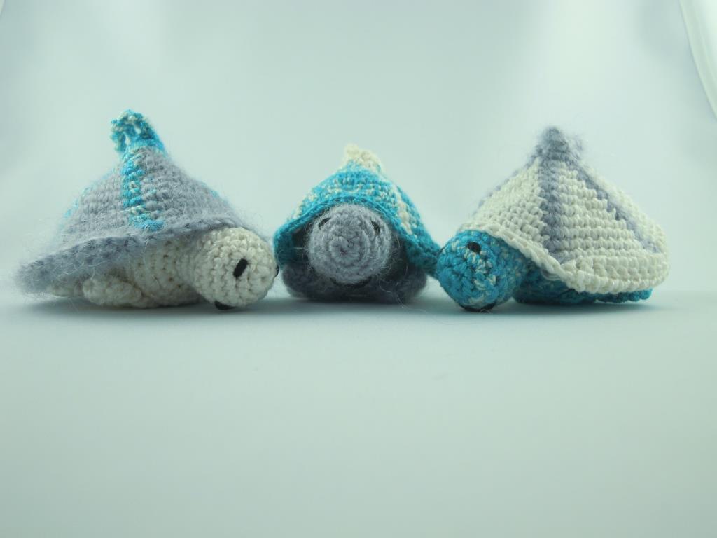 Drei gehäkelte Amigurumi-Schildkröten in Blau-, Grau- und Cremetönen auf hellem Untergrund.